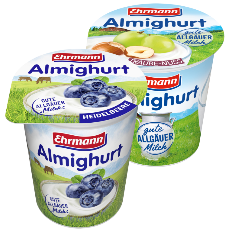 Zu sehen sind zwei Joghurtbecher der Marke "Ehrmann Almighurt" mit je 150g. Links abgebildet die Sorte Heidelbeere und rechts die Traube-Nuss. Auf den Deckeln, sowie den Joghurtbechern selbst, ist das Ehrmann Almighurt Logo abgebildet, sowie ein Aufkleber mit der Aufschrift "Gute Allgäuer Milch". Je eine Schüssel mit Joghurt und Heidelbeeren und eine Schüssel mit Trauben und Nüssen sind auf den einzelnen Bechern zu sehen. Die Schüsseln stehen auf einer grünen Kuhweide.